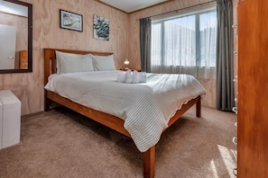 A bedroom with a wooden bed, a bedside table, a lamp, and a window with curtains.