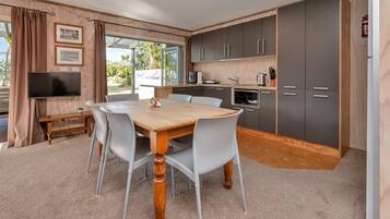 A modern kitchen with grey cabinets, a wooden dining table, and a TV in the living area.