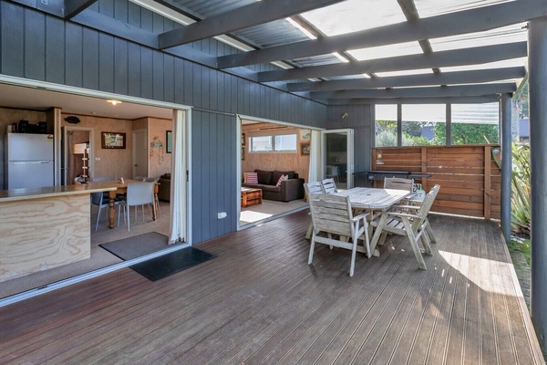 The large covered timber deck features a gas BBQ and dining table, perfect for meals in any weather.