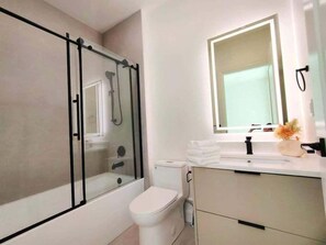 A modern bathroom with a glass-enclosed shower, a toilet, and a sink with a mirror.
