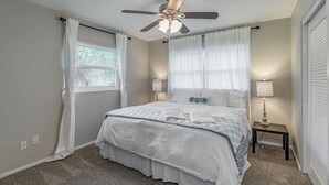 Une chambre à coucher avec un lit, un ventilateur de plafond, des lampes de chevet et une fenêtre avec des rideaux.