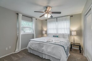 Ein Schlafzimmer mit Bett, Deckenventilator, Nachttischlampen und einem Fenster mit Vorhängen.
