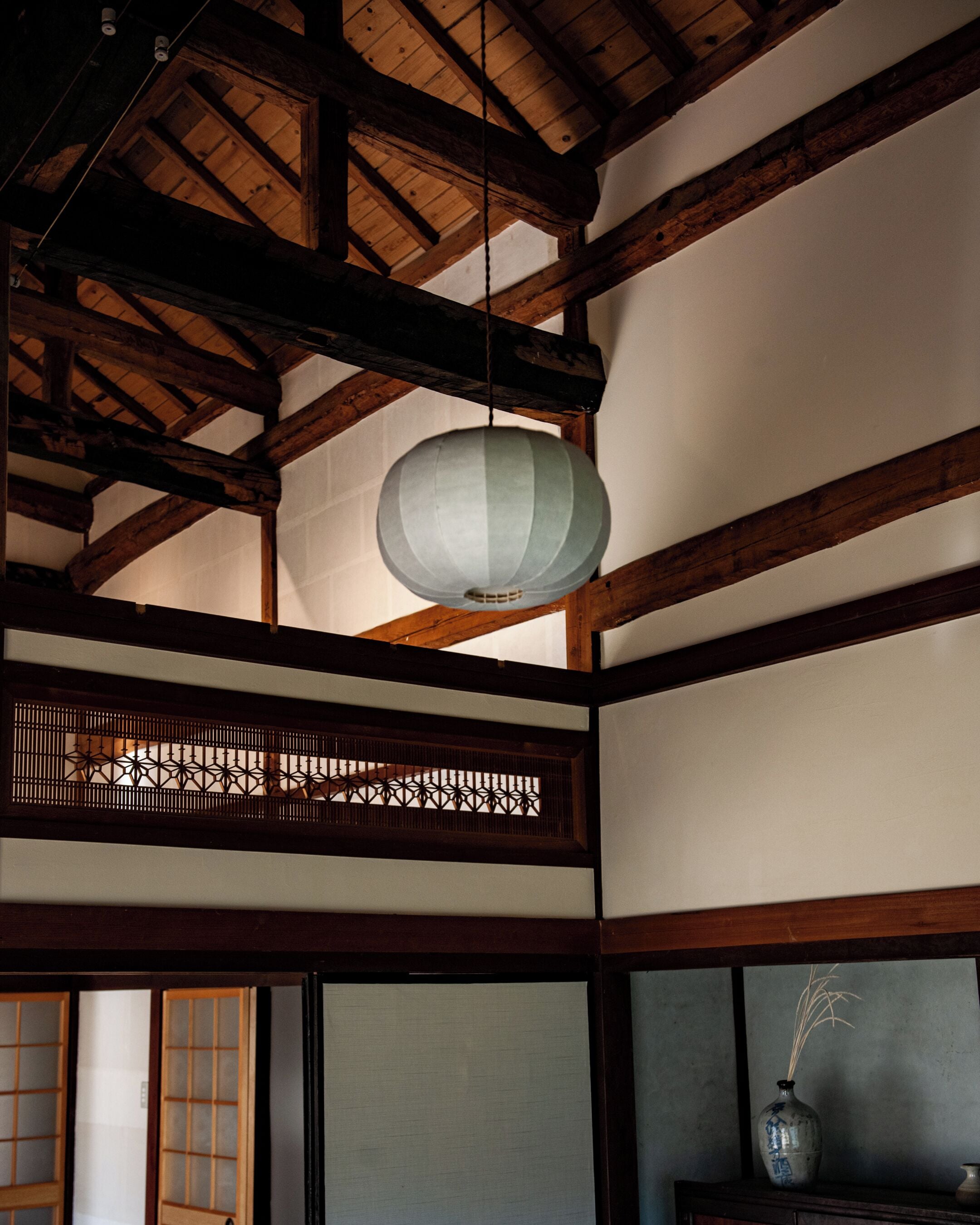 A traditional Japanese room with wooden beams, tatami flooring, a shoji screen, and a hanging paper lantern.