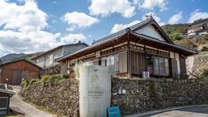 A traditional Japanese house with a stone wall, a concrete sign with a map, and a clear sky. - entohouse BAR&GUESTHOUSE (Seiyo)