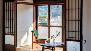 A traditional Japanese room with tatami flooring, a sliding door, a table with a vase, and a chair. - entohouse BAR&GUESTHOUSE (Seiyo)