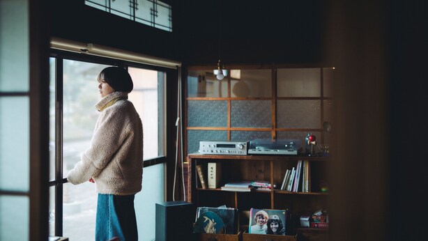 A person standing by a window in a room with a wooden bookshelf and a radio. - entohouse BAR&GUESTHOUSE (Seiyo)