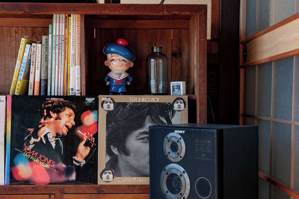 Un mueble de madera con libros, una figurita y un altavoz negro grande.