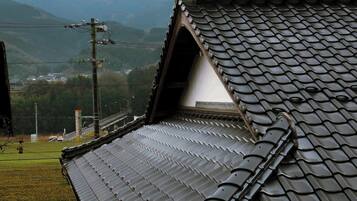 A traditional building with a sloped roof, a visible chimney, and a view of a hilly landscape in the background.