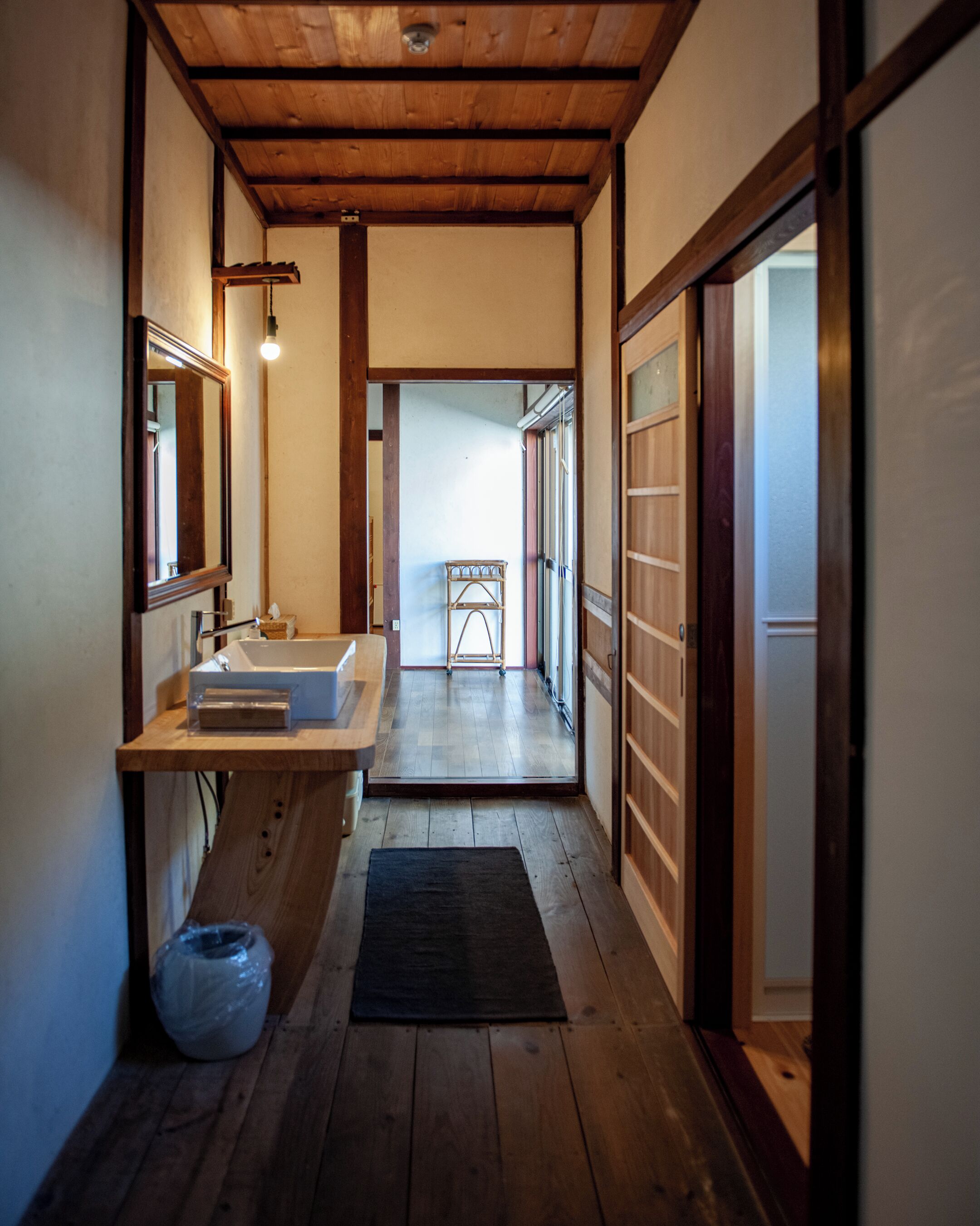 A narrow hallway with wooden flooring, a sink, and a mirror.