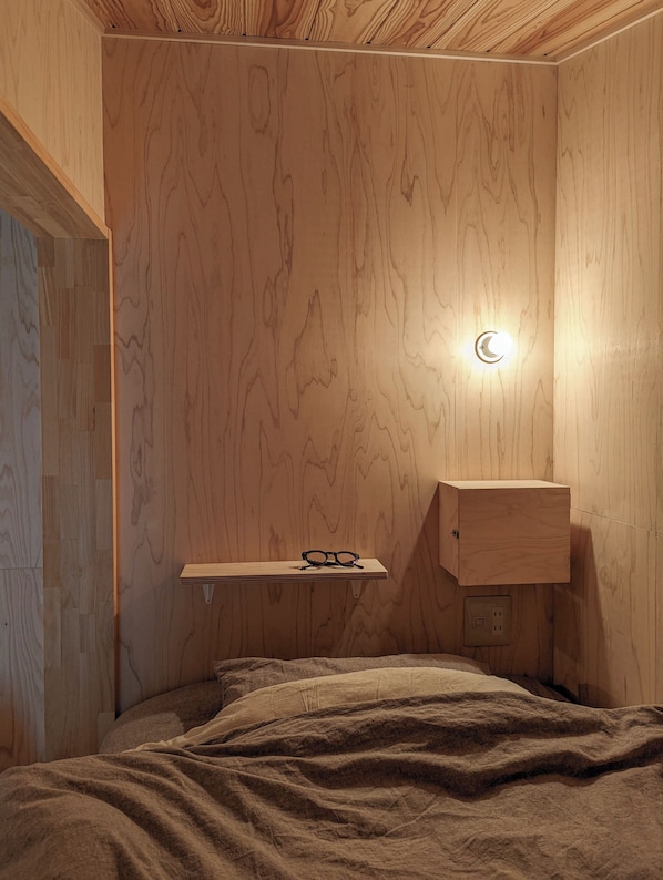 Un dormitorio con paneles de madera, una mesita de noche con vasos, una lámpara de pared y una mesita auxiliar.