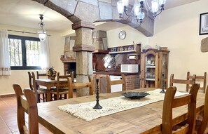 A dining area with a wooden table, chairs, a chandelier, and a stone fireplace. - APARTBEACH OASIS YOUR PARADISE WITH TROPICAL POOL, JACUZZI (RIUDOMS)