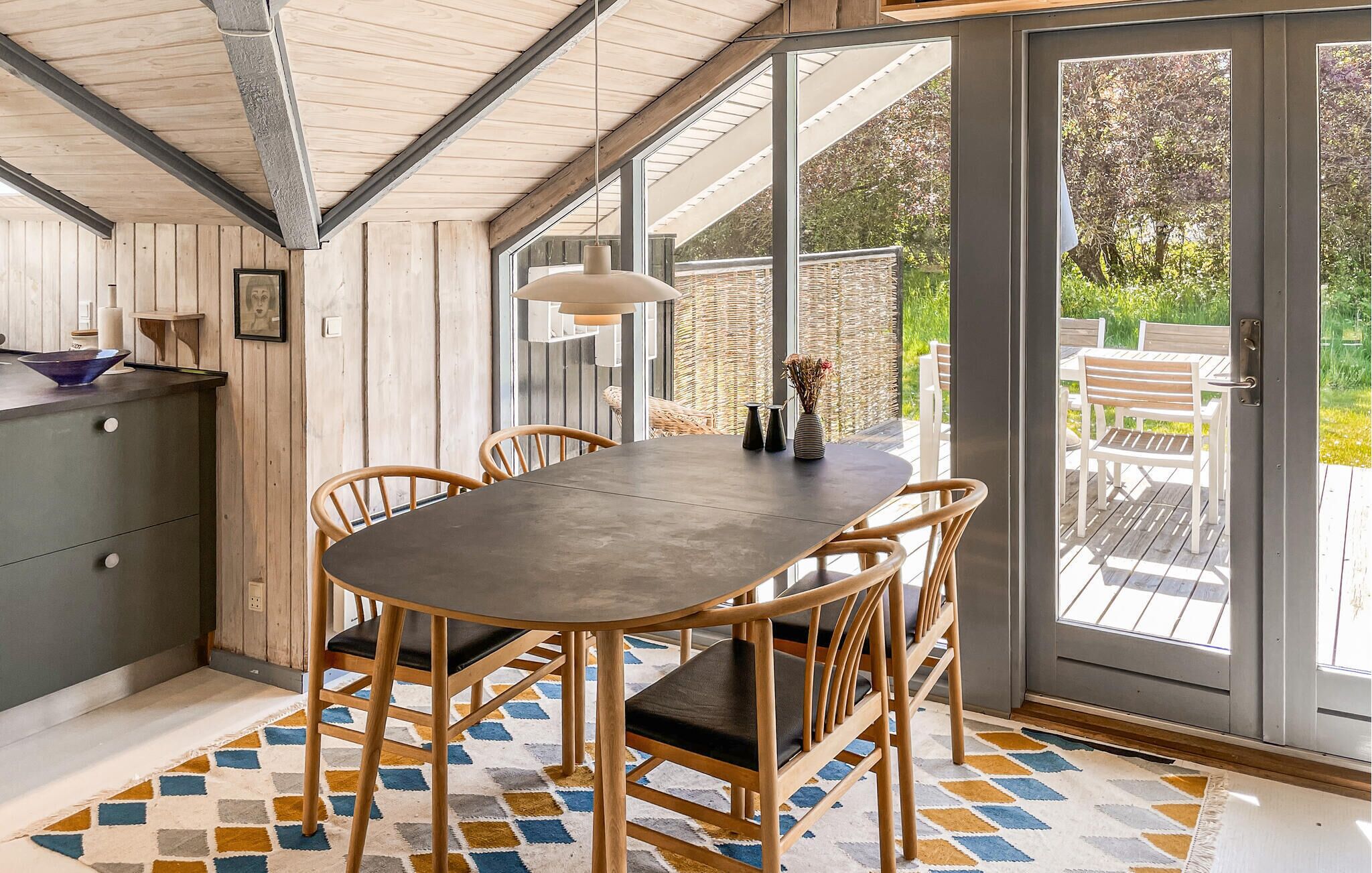 A dining area with a table and chairs, a kitchen counter, and a large window with a view of greenery.