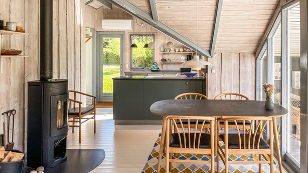 Una cocina moderna con una isla central, una zona de comedor con mesa y sillas, y una estufa de leña.