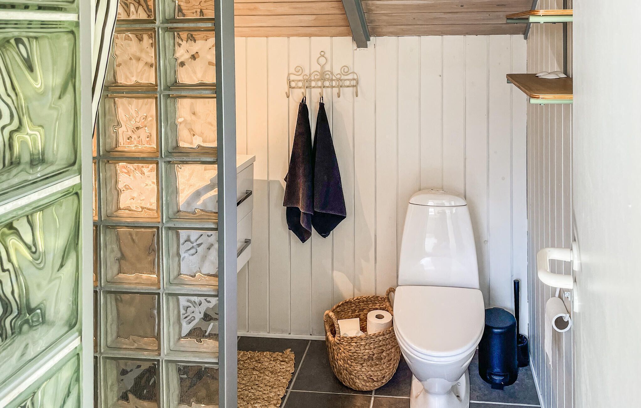 A bathroom with a toilet, a hanging towel rack, a basket with toiletries, and a wooden door with a glass panel.