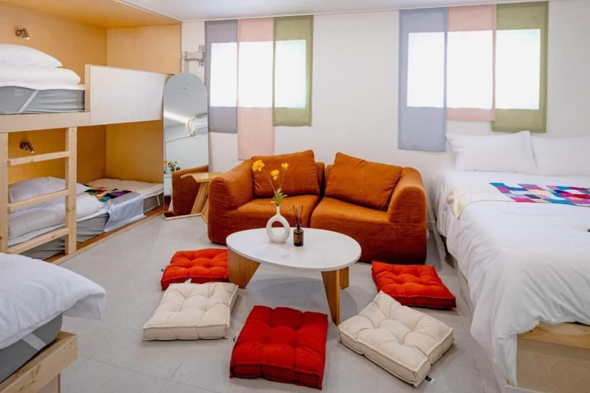 Une chambre moderne avec des lits superposés, un canapé, une table basse et un lit recouvert d’une couverture aux couleurs vives.