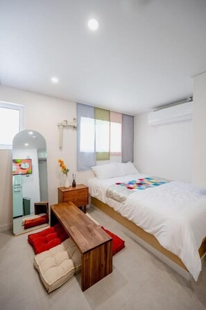 A modern bedroom with a bed, a wooden nightstand, a bench, and a TV.
