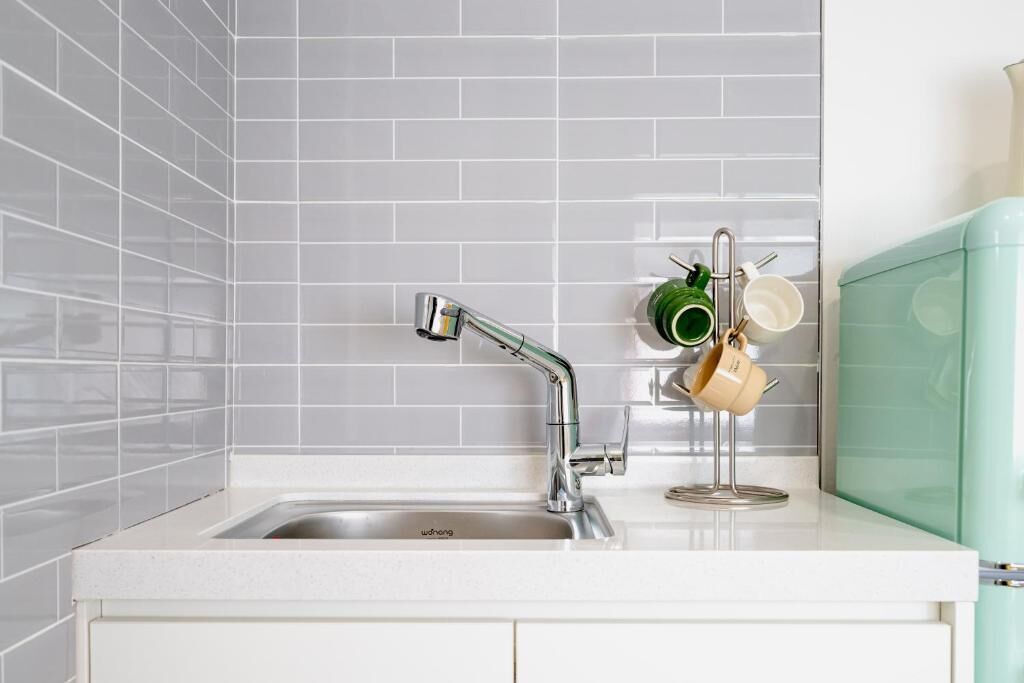 A kitchen with a stainless steel sink, white tiled backsplash, and a green appliance.