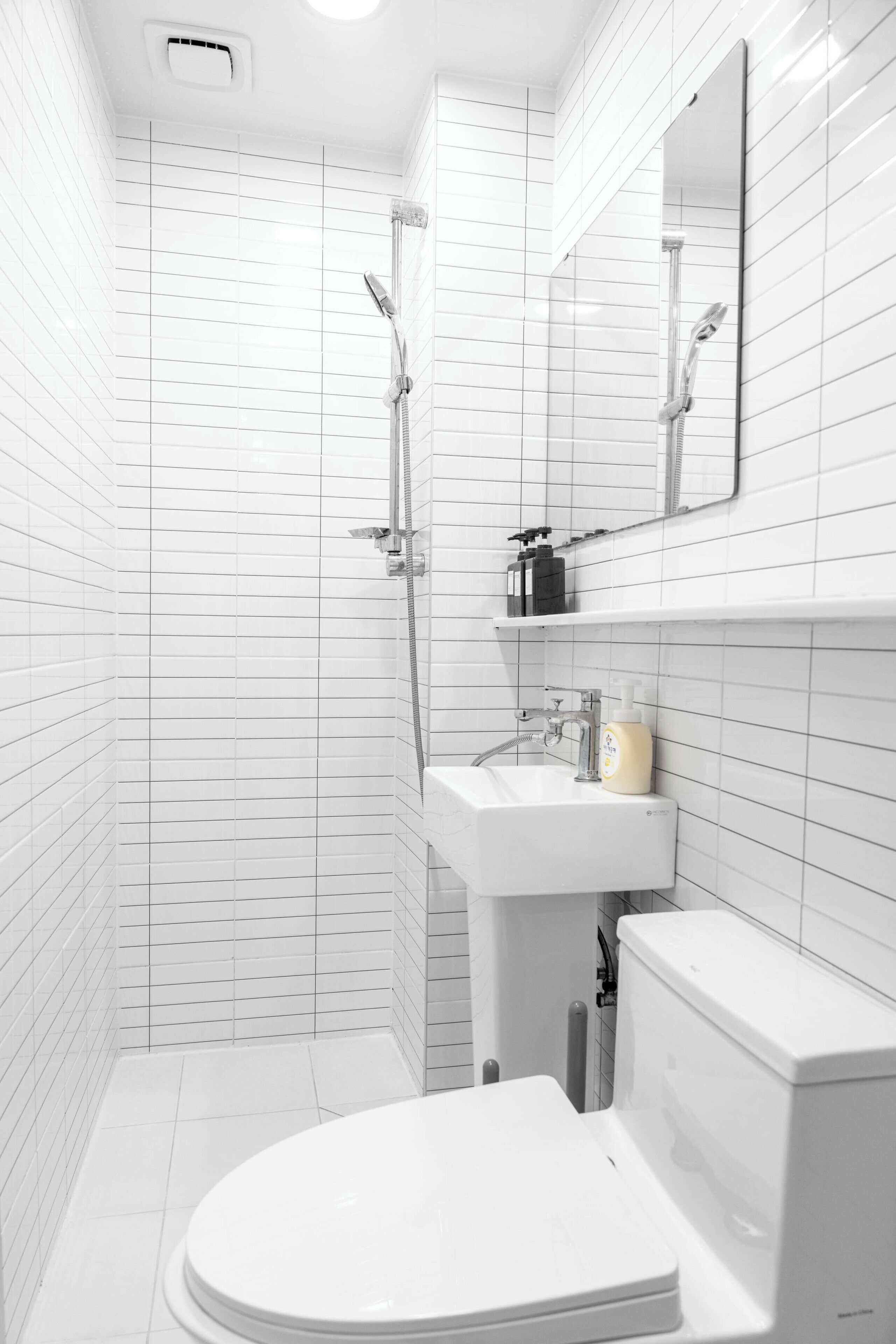 A bathroom with white tiled walls, a white sink, a toilet, and a shower area.
