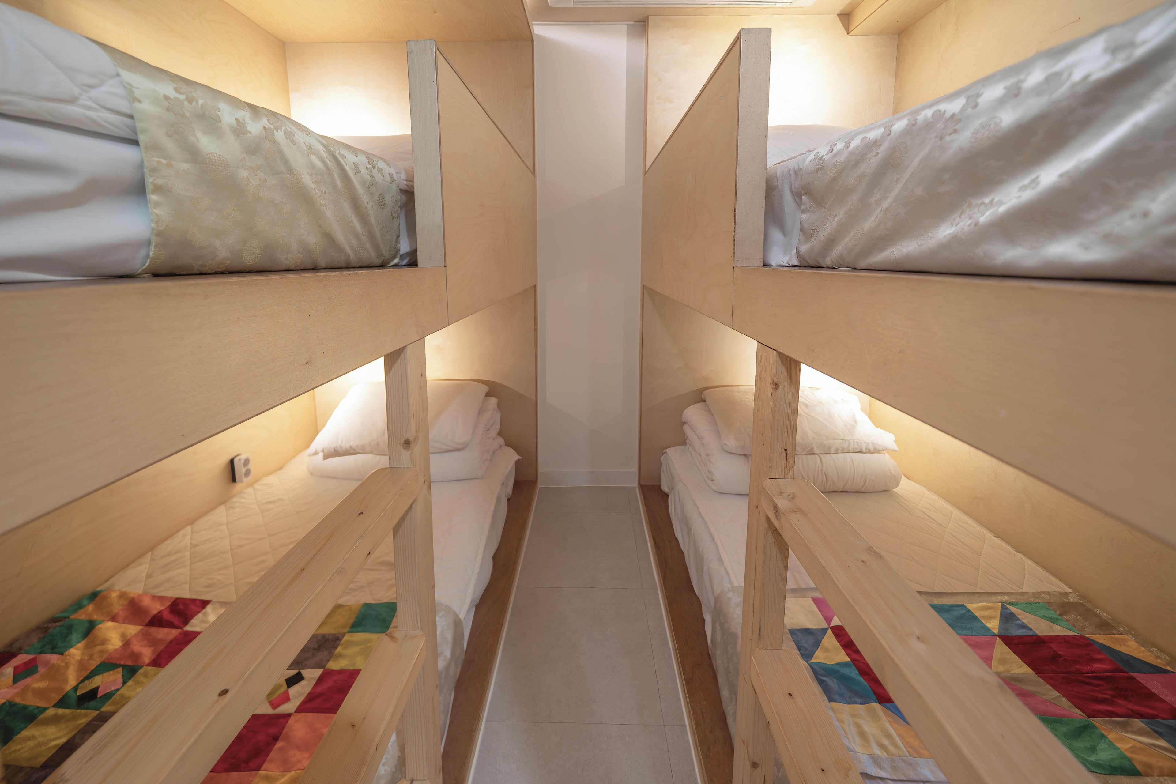A narrow corridor with bunk beds on either side, each with a quilted mattress and a pillow.