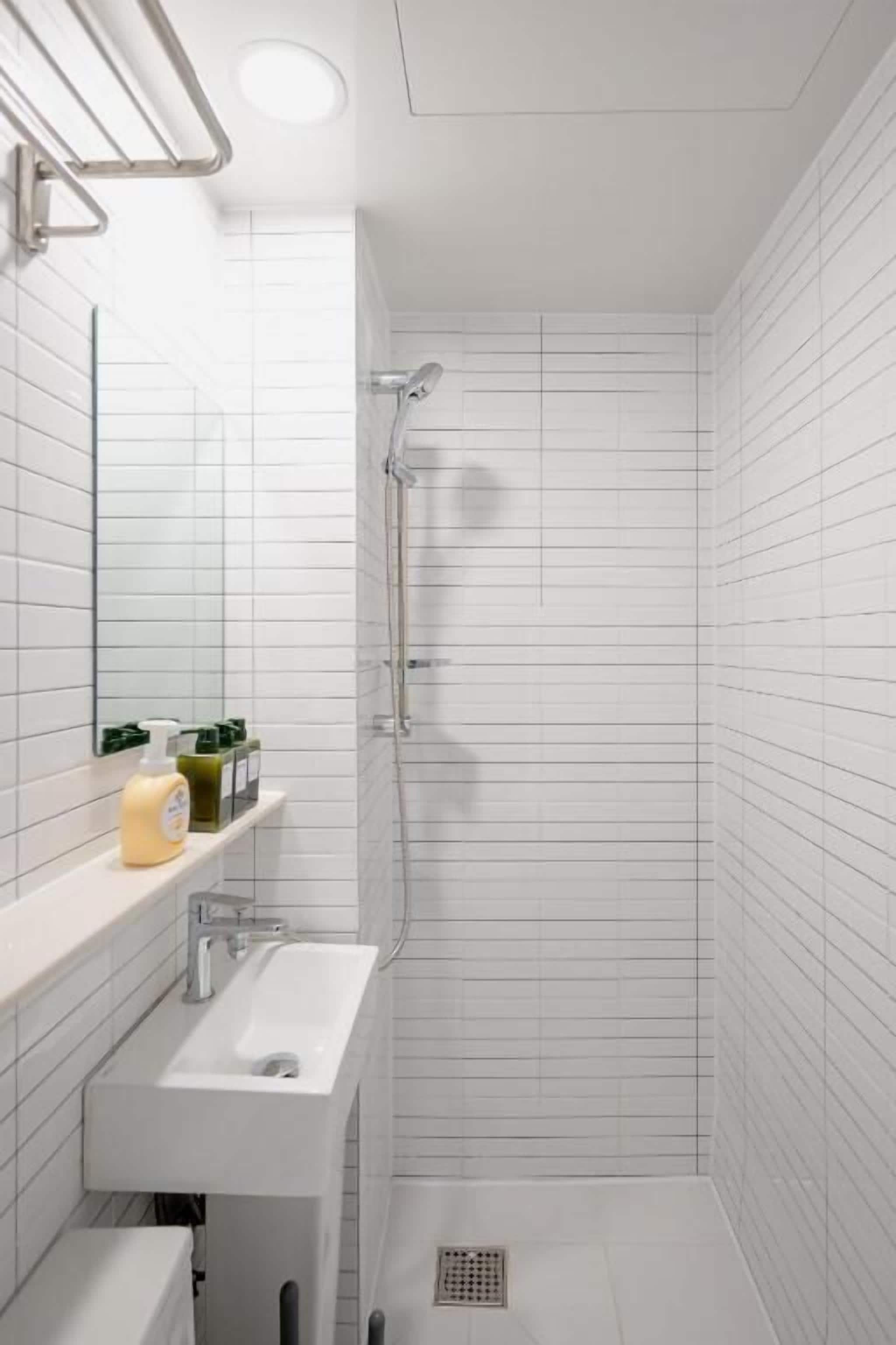 Ein modernes Badezimmer mit weißen Fliesen, einem Waschbecken und einer Dusche.