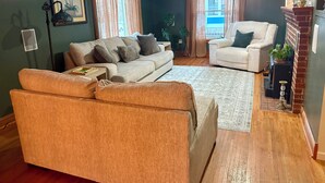 Un salon comprenant un canapé, des fauteuils, une table basse, une cheminée et une fenêtre avec des rideaux.
