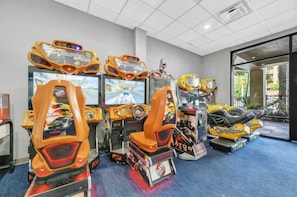 A row of arcade racing game machines in a room with a blue carpet. - 2BR Condo 7 mins to Disney | FREE Resort Access (Orlando)