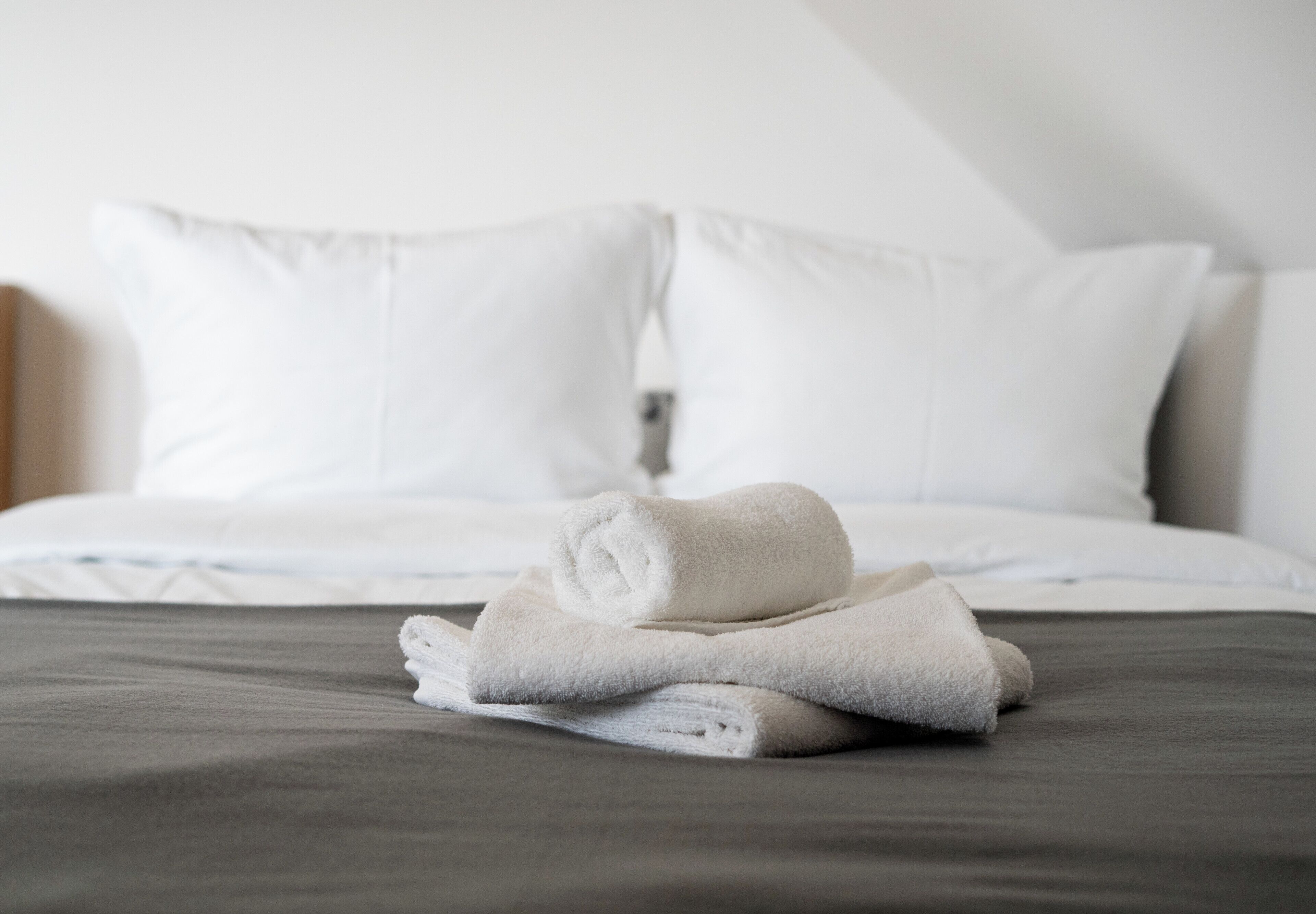 A neatly made bed with white pillows and a folded white towel on a dark-colored bedspread.
