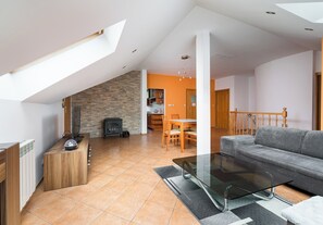 Un salon moderne avec une table basse en verre, un canapé gris, un coin repas avec une table et des chaises en bois, et une cuisine en arrière-plan.