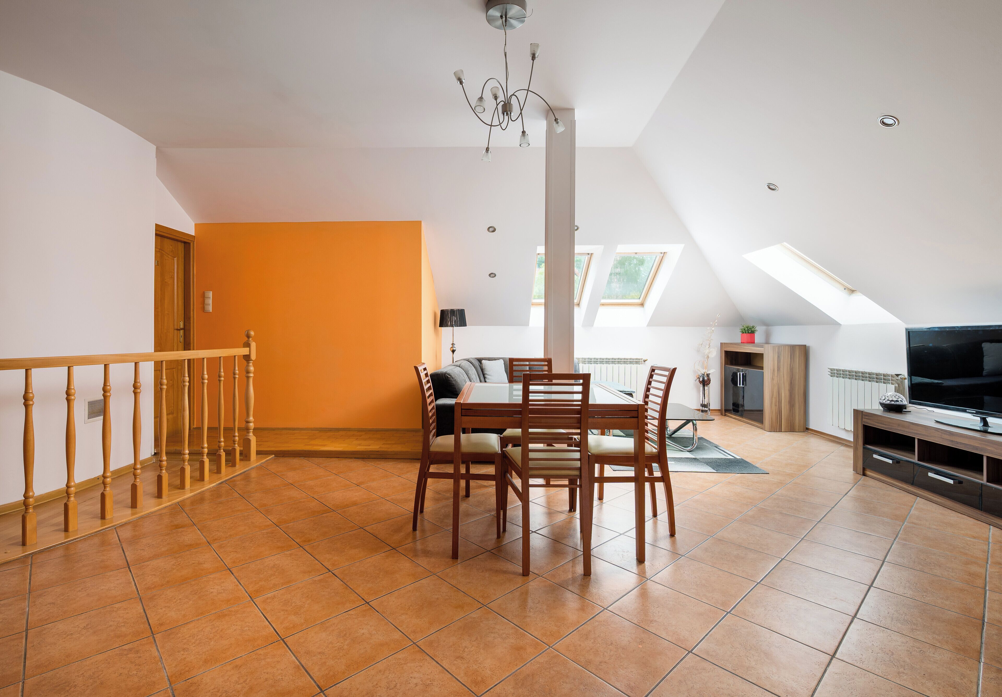 A spacious living area with a dining table, chairs, a TV, and a staircase leading to an upper level.