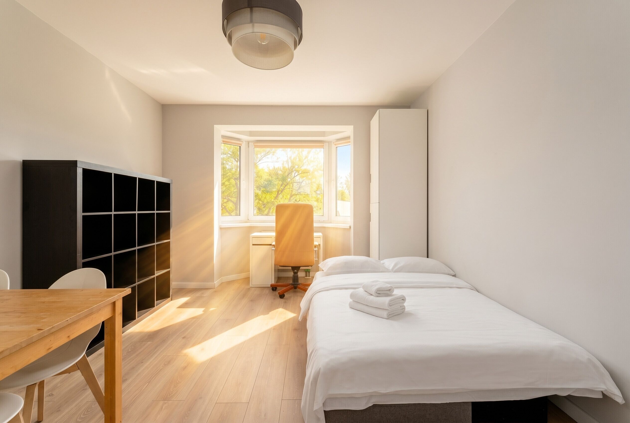 A bedroom with a bed, a desk, a chair, a wardrobe, and a window.