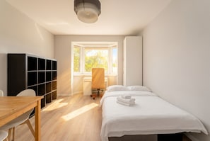 Ein Schlafzimmer mit Bett, Schreibtisch, Stuhl, Kleiderschrank und Fenster.