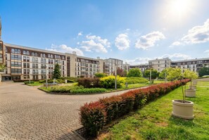 A modern building complex with a paved courtyard, landscaped gardens, and a clear sky. - Cracow Royal Charm Apartment (Kraków)