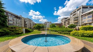 A swimming pool with a fountain, surrounded by greenery and residential buildings.