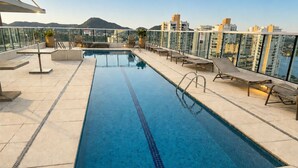 Una piscina en la azotea con agua cristalina y azul, rodeada de sillones de descanso y una barandilla de cristal.