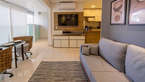 Una sala de estar moderna con sofá, televisión, comedor con sillas, zona de cocina y obras de arte en la pared.