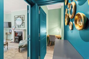 A teal-walled room with a fireplace, a desk, and a bed. - Marine Splendour with Sea View | 2 Bed, 2 Bath (Brighton and Hove)