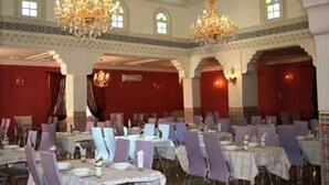 A banquet hall with tables set for dining, chandeliers, and arched windows.