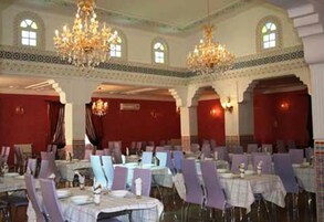 Un salón de banquetes con mesas dispuestas para comer, candelabros y ventanas arqueadas.
