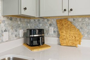 A kitchen with white cabinets, a black coffee maker on a wooden tray, and a Georgia-themed wall decoration. - KingBeds+Base10min+Hwy84+ChefKitchen+Spa Showers (Hinesville)