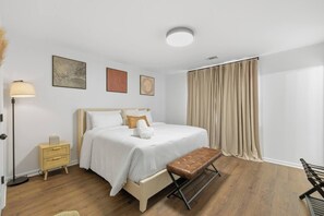 A bedroom with a bed, bedside table, lamp, bench, and curtains.