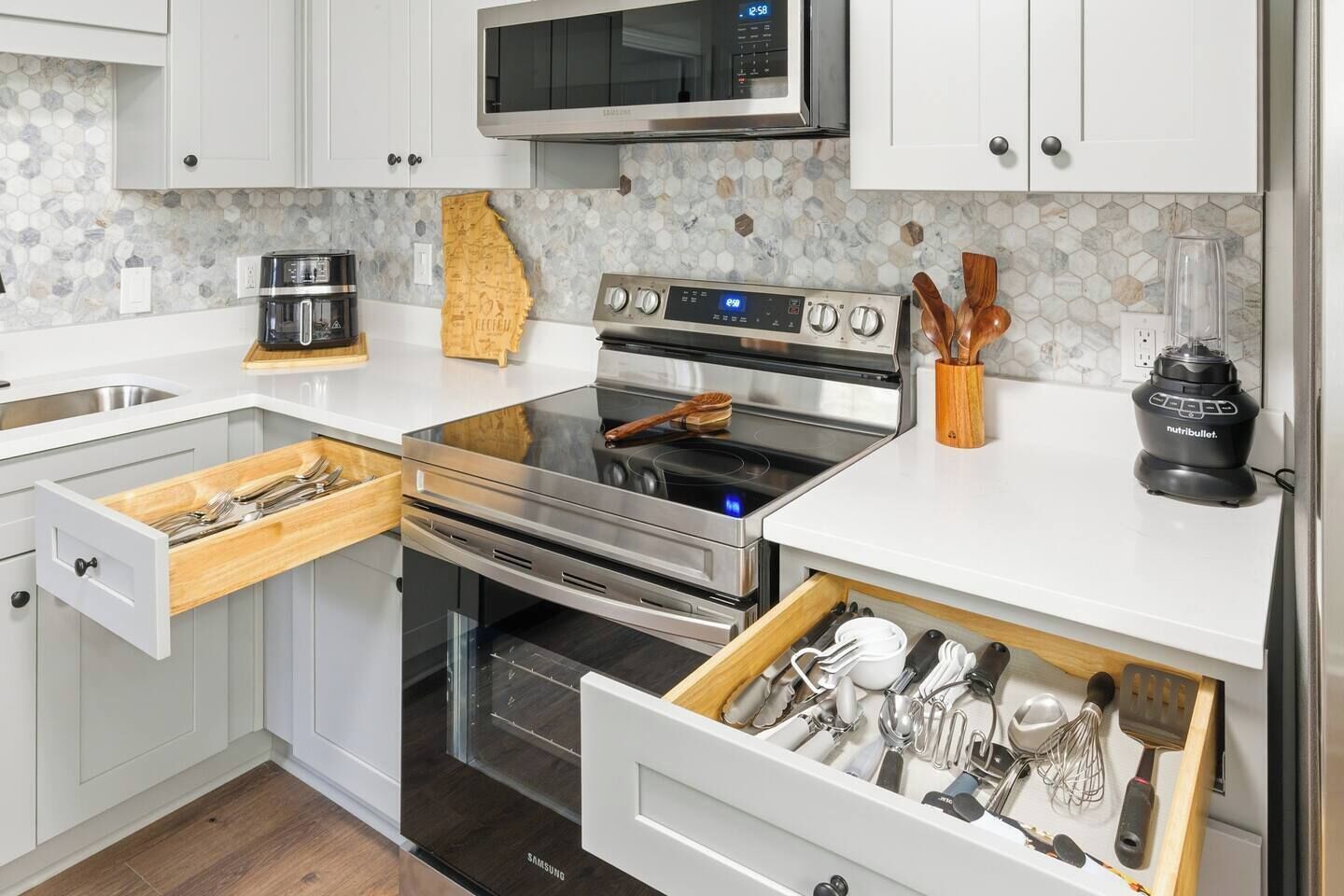Una cocina moderna con armarios blancos, una estufa de acero inoxidable, un horno, un microondas y un cajón con utensilios.