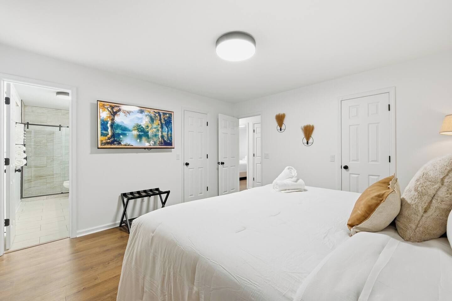 A hotel room with a large bed, a painting on the wall, and a door leading to a bathroom.