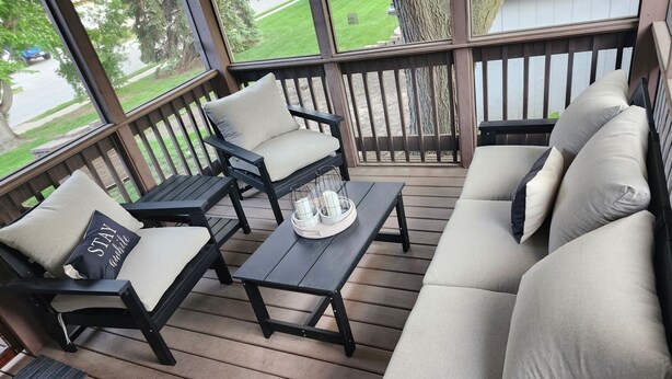 Ett takförsett utomhusområde med sittplatser, bestående av en soffa, stolar och ett bord, med utsikt över en bostadsgata.