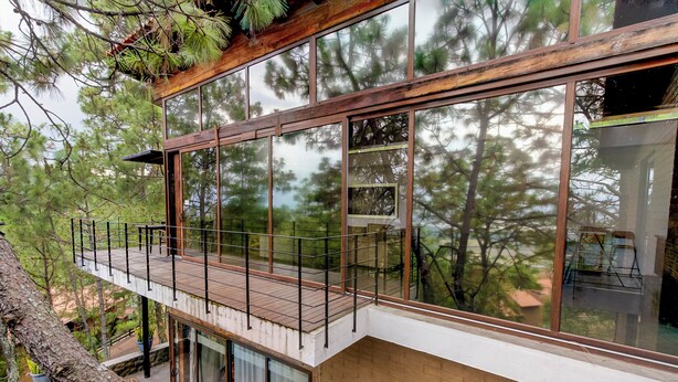 A modern building with large windows, a wooden deck, and a view of trees.