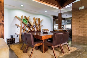 Un coin repas avec une table en bois et des chaises en cuir, une bibliothèque et, au fond, une cuisine.
