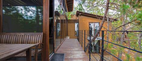Una terraza de madera con un banco, una puerta de cristal y vistas a árboles.