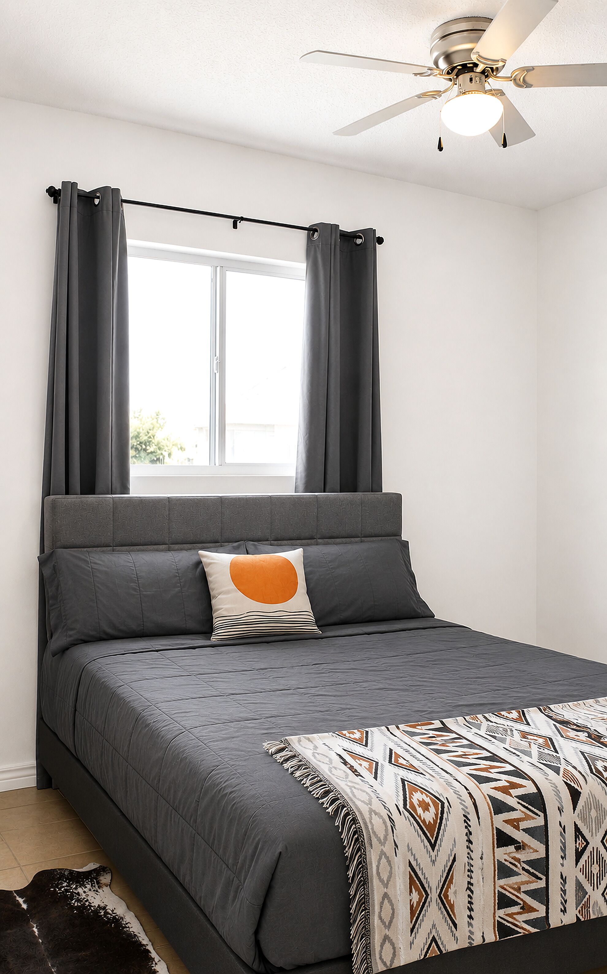 A bedroom with a bed, curtains, a ceiling fan, and a window.