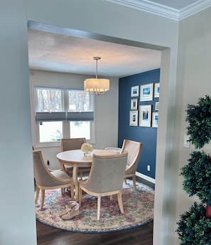 A dining area with a round table, four chairs, a chandelier, and a patterned rug.