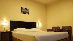 A hotel room with a large bed, two bedside lamps, a small table, and a chair. - Jatinangor Hotel Restaurant (Cileunyi)