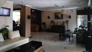 A modern living room with a sofa, coffee table, and a TV. There are plants, a painting, and a cabinet. - Jatinangor Hotel Restaurant (Cileunyi)